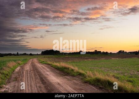 Sandigen Weg durch Felder, Horizont und Wolken am Himmel nach Sonnenuntergang Sommerabend anzeigen Stockfoto