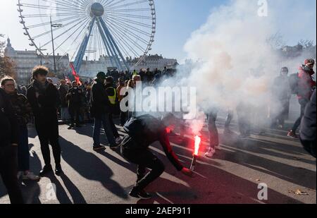 Lyon, Frankreich. 10 Dez, 2019. Ein Demonstrant zündet Feuerwerk während einer Demonstration im Rahmen der Streiks und Proteste gegen die Rentenreform in Frankreich auf Platz Bellecour. Den Generalstreik und gewalttätigen Protesten in Lyon halten auch die Fans des Fußball-Erstligisten RB Leipzig auf Ihren Zehen. Um 12.00 Uhr am Dienstag, dem Club warnte seine Anhänger nicht an der Place Bellecour für eine gemeinsame Fahrt zum Stadion zu treffen. Kurz danach gab es massive Auseinandersetzungen zwischen Demonstranten und der Polizei auf und um den Platz. Quelle: dpa Picture alliance/Alamy leben Nachrichten Stockfoto