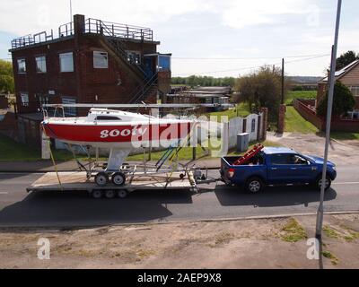 Eine kleine Racing Yacht von Straße auf einem Tieflader mit einem 4x4 Pickup truck transportiert. Stockfoto