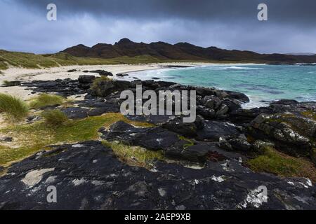 Dramatische Himmel über Sanna Bay an der Westküste von Schottland, Großbritannien. Sandstrand, türkisblaues Meer, Gebirge im Hintergrund und schwarzen vulkanischen Basaltgestein. Stockfoto