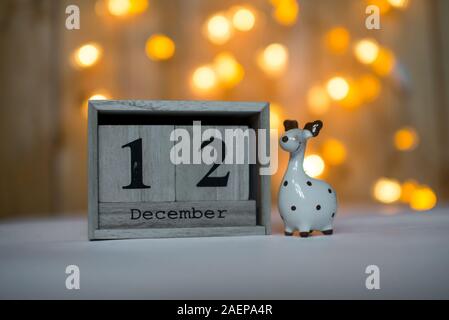 Cube Holz- Kalender mit Datum am 12. Dezember mit keramischen Rentier Figur über bokeh Hintergrund. Adventskalender, Weihnachten Hintergrund Stockfoto