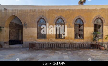 Reihe von vier angrenzenden hölzernen grunge Bogenfenster mit verzierten schmiedeeisernen Gitter über gelb Stein Ziegel Wand, holzbalustrade und Eingang der gewölbten Durchgang, mittelalterliche Kairo, Ägypten Stockfoto