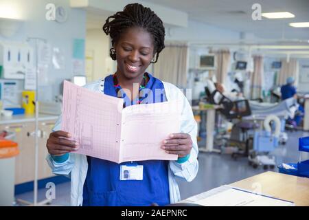 Eine NHS Krankenschwester in einem Krankenhaus Kontrollen fest, dass Patienten das NHS noch mehr unter Druck durch hohe Anforderungen und Haushaltskürzungen fühlt. Stockfoto