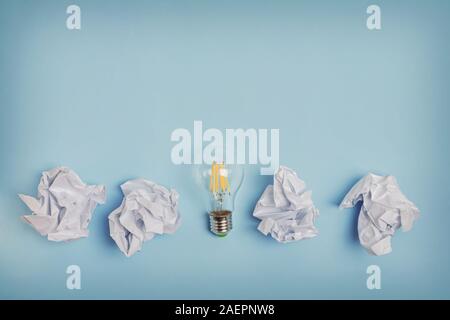 Zerknittertes Papier und Glühbirne auf dem blauen Hintergrund. Stockfoto