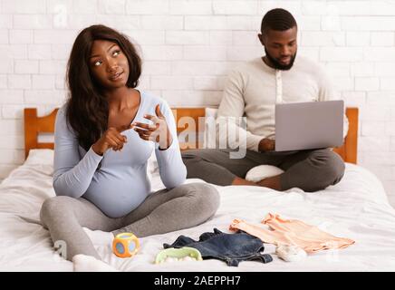 Schöne schwangere Frau Vorbereitung Babykleidung, Mann mit Laptop Stockfoto