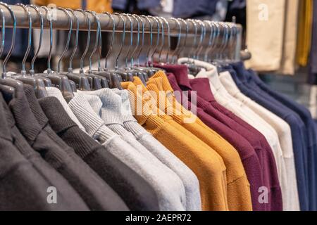 Strickjacken und Pullover in verschiedenen Farben, Schwarz, Grau, Weiß und Rot auf einem Kleiderbügel in einem Bekleidungsgeschäft in einer Reihe hängen. Herbst und Winter saison c Stockfoto