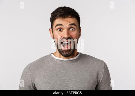 Außerordentlich froh und heiter gut aussehender Bärtiger kaukasischen Mann in grauen Pullover, offenen Mund fasziniert, sagen wow überrascht und amüsiert, besuchen Sie Stockfoto