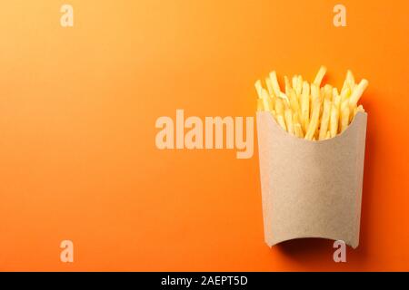 Scheiben heiße Pommes frites in Box auf orangem Hintergrund, Platz für Text. Ansicht von oben Stockfoto