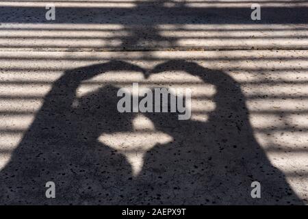 Silhouette von ein paar mit ihren Köpfen zusammen bilden eine Herzform mit ihren Armen wirft einen Schatten auf den Bürgersteig mit Gitter Overhead Stockfoto