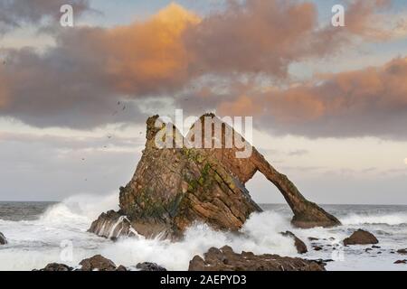 Bogen GEIGE ROCK PORTKNOCKIE Küste von Moray in Schottland stürmischen WINTER SONNENUNTERGANG MIT ORANGE farbige Wolken und einem aufgehenden Mond Stockfoto