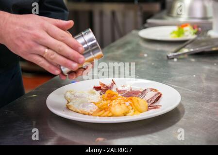 Gewürz von einem Teller die Eier mit Schinken und Kartoffeln zu, die ein wenig Paprika aus La Vera hinzugefügt wird. Stockfoto