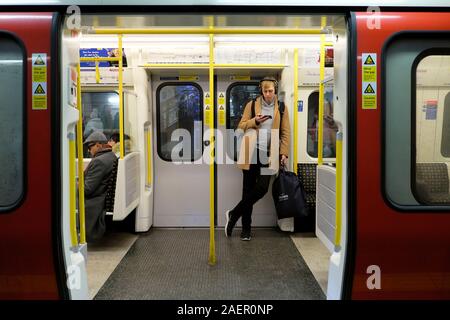 Junge Mann in U-Bahn Wagen mit offenen Türen warten auf eine U-Bahn station Plattform auf Handy London UK KATHY DEWITT Stockfoto