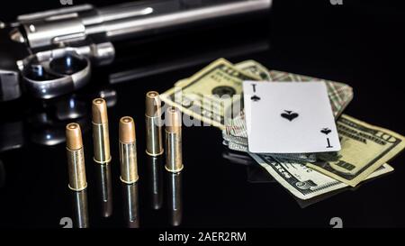 Gefährliches Glücksspiel für Geld. Eine Pistole mit Patronen, Geld Dollar und ein Deck Spielkarten mit einem Ace of Spades liegen auf einem Glastisch. Dangerou Stockfoto