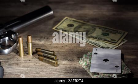 Gefährliches Glücksspiel für Geld. Eine Pistole mit Patronen, Geld Dollar und ein Deck Spielkarten mit einem Ace of Spades liegen auf einem Holztisch. Dangero Stockfoto