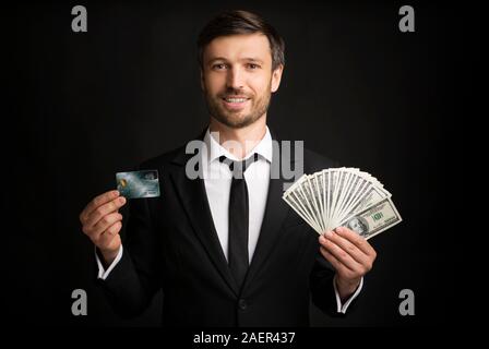 Geschäftsmann mit Kreditkarte und Geld über schwarzen Hintergrund stehend Stockfoto