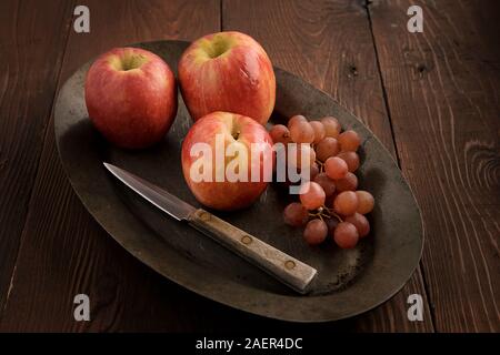 Eine Nahaufnahme von Äpfeln und roten Trauben mit einem Messer auf einer kleinen Platte. Stockfoto