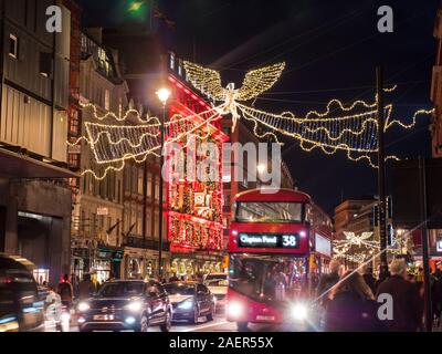 Weihnachten Piccadilly bei Nacht mit Fortnum & Mason Store beleuchtet mit Adventskalender Thema und roten hybrid London Bus, Einkäufer und Verkehr mit Weihnachten Goldener Engel lights Illuminationen Piccadilly London UK Stockfoto