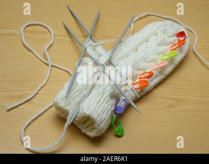 Weißen Handschuh- und Stricknadeln auf hölzernen Hintergrund Stockfoto