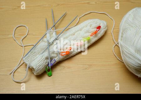 Weiße Handschuhe und Stricknadeln, Ball der Wolle auf Holz- Hintergrund Stockfoto