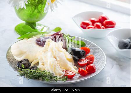 Traditionelle weiße weiche faserige Cecil Käse liegt auf einer Platte. Der Käse wird mit reifen Tomaten und Oliven eingerichtet. Stockfoto