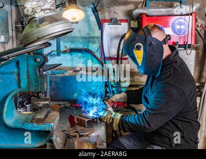 Elektrischen Schweißverfahren. Arbeiter in Schweißen Maske. Gelbe Funken fliegen zu den Seiten. Helles Weiß und Blau. Stockfoto