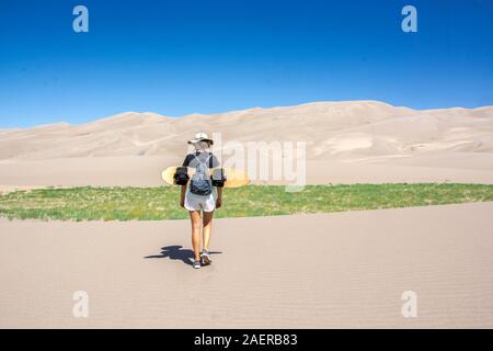 Junge Frau mit Sand board Fuß in Richtung der Dünen im Great Sand Dunes National Park, Colorado, Vereinigte Staaten von Amerika Stockfoto