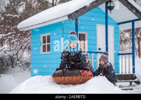 Glückliche Kinder Rodeln im Winter im Hof. Drei kleine Kinder in warmen Overalls spielen draußen auf frostigen Wintertag. Drei Brüder nehmen Schlittenfahrt wiederum Stockfoto