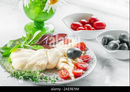 Traditionelle weiße weiche Faser Cecil Käse in der Form eines Pigtail liegt auf einer Platte. Käse ist mit Scheiben von reifen Tomaten und Oliven eingerichtet. Stockfoto