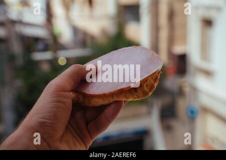 Weißes Brot Sandwich mit Brummen und Salat in der Hand des Menschen in Monaco Stockfoto