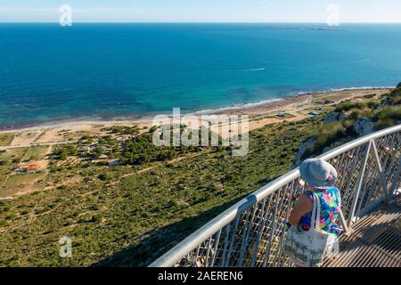 Frau mittleren Alters tragen ein Sonnenhut auf den Blick von der Santa Pola Skywalk Aussichtsplattform auf den Klippen oberhalb Partida Bancal de la Arena, EIN Stockfoto