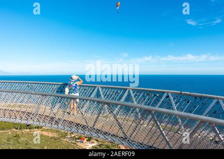 Frau mittleren Alters tragen ein Sonnenhut auf den Blick von der Santa Pola Skywalk Aussichtsplattform auf den Klippen oberhalb Partida Bancal de la Arena, EIN Stockfoto