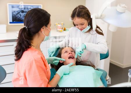 Adorable Kinder Zahnarzt in der zahnärztlichen Chirurgie mit zwei hübschen Mädchen zeigen Ihnen zahnmedizinische Check-up, ein Mädchen ist Assistent spielen Stockfoto