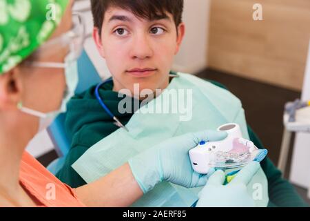 Close-up des jungen Mannes in der zahnärztlichen Chirurgie auf die Ärztin, die zeigt, wie die Zähne zu putzen, Zahnpflege Konzept Stockfoto