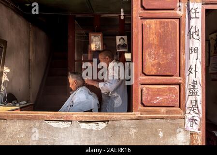 März 14, 2019: ein Friseur schneiden die Haare von einem älteren Mann in Xizhou, Yunnan, China Stockfoto