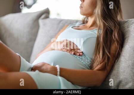 Im mittleren Abschnitt der besorgt schwangere Frau im Sofa mit ihren Händen am Bauch Stockfoto
