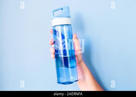 Hält eine Frau blaue Flasche Wasser in der Hand, für den Sport. Auf einem hellen Hintergrund. Gesunder Lebensstil und Fitness Concept im klassischen 2020 Farbe des Ja Stockfoto