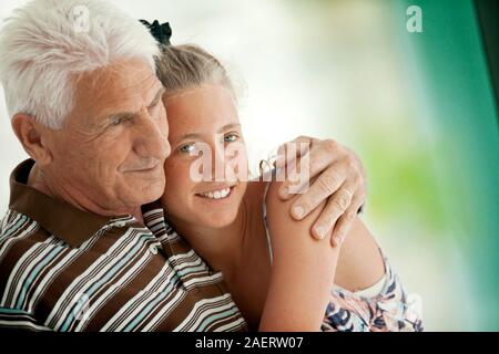 Junges Mädchen lächeln, da sie umarmt ihr Großvater, während Sie für ein Portrait darstellen. Stockfoto