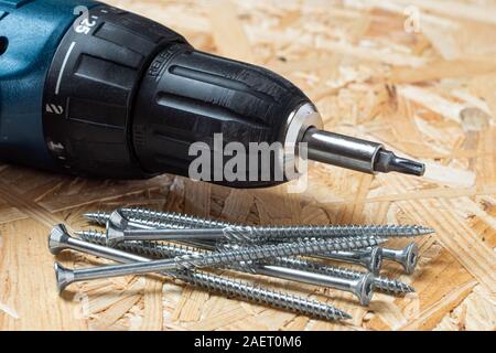 Elektrische Schraubendreher mit Torx Bit und selbst bohren Schrauben liegen auf Chip board. Unscharfer Hintergrund. Stockfoto