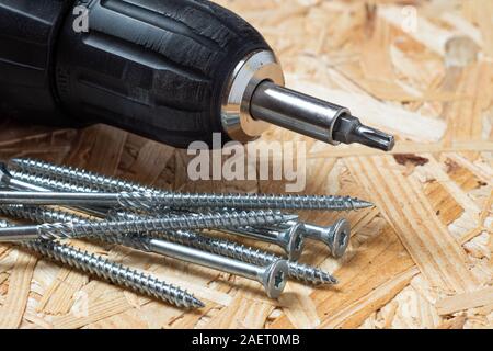 Elektrische Schraubendreher mit Torx Bit und selbst bohren Schrauben liegen auf Chip board. Unscharfer Hintergrund. Stockfoto