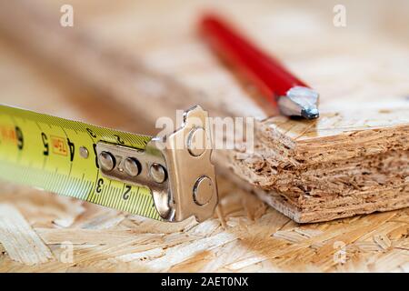 Ein Tipp des gelben Metalls Maßband und roten Zimmermanns Bleistift liegen auf Chip board. Unscharfer Hintergrund. Stockfoto