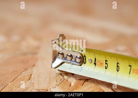 Ein Tipp des gelben Metalls Maßband liegen auf Chip board. Unscharfer Hintergrund. Stockfoto