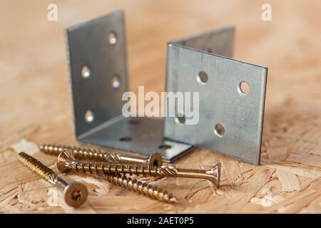 Zwei verzinkte Winkel und selbst bohren Schrauben liegen auf Chip board. Unscharfer Hintergrund. Stockfoto