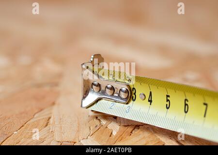 Ein Tipp des gelben Metalls Maßband liegen auf Chip board. Unscharfer Hintergrund. Stockfoto