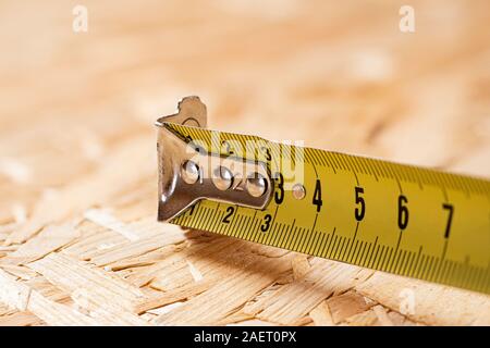 Ein Tipp des gelben Metalls Maßband liegen auf Chip board. Unscharfer Hintergrund. Stockfoto