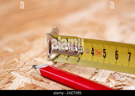 Ein Tipp des gelben Metalls Maßband und roten Zimmermanns Bleistift liegen auf Chip board. Unscharfer Hintergrund. Stockfoto