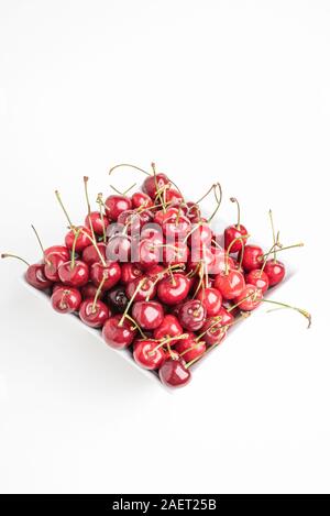 Ein Bündel von frischen roten Kirschen angeordnet und in einem quadratischen Porzellan Schüssel auf weißem Hintergrund. Stockfoto