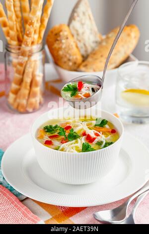 Weiße Schüssel mit frischen, hausgemachten Hühnersuppe, französisch Laib und Brot klebt auf einem Tisch Stockfoto