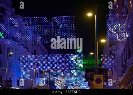 Ein Blick entlang einer befahrenen Gran Via in Madrid, beleuchtet mit Weihnachtsbeleuchtung einschließlich Katzen und der Telefonica Gebäude in Grün beleuchtet Stockfoto