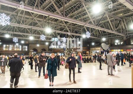 Die Passagiere stehen, sitzen und gehen, die sich um die voll geschmückten Weihnachtsbaum in der Mitte der Bahnhofshalle Hauptbahnhof Glasgow, Glasgow, Schottland Stockfoto