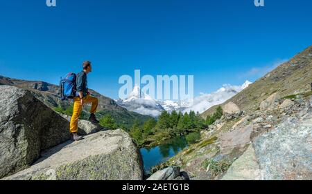 Wanderer steht auf Felsen und in die Ferne schaut, hinter dem See Grindij und Schnee - Matterhorn, Wallis, Schweiz abgedeckt Stockfoto